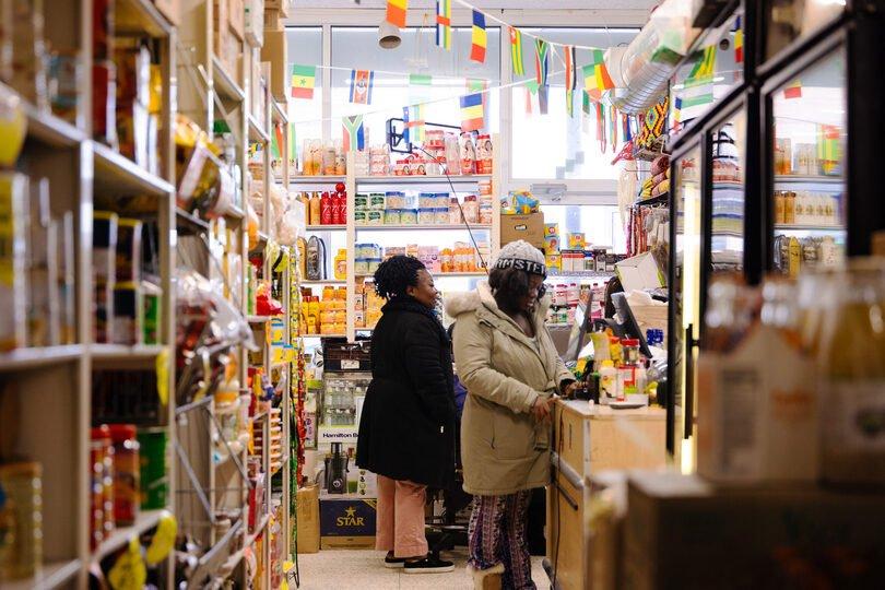 Inside Safari Supermarket: a shopper at the counter, aisles of imported goods and a row of flags overhead